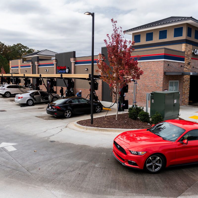 A red sports car exits Big Dan's automatic soft-touch car wash in Woodstock, GA, looking radiant, shiny, and clean