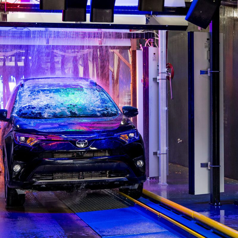 Black vehicle receives a spotless rinse in Big Dan's soft-touch automatic car wash, pulled along a track and illuminated by neon lights