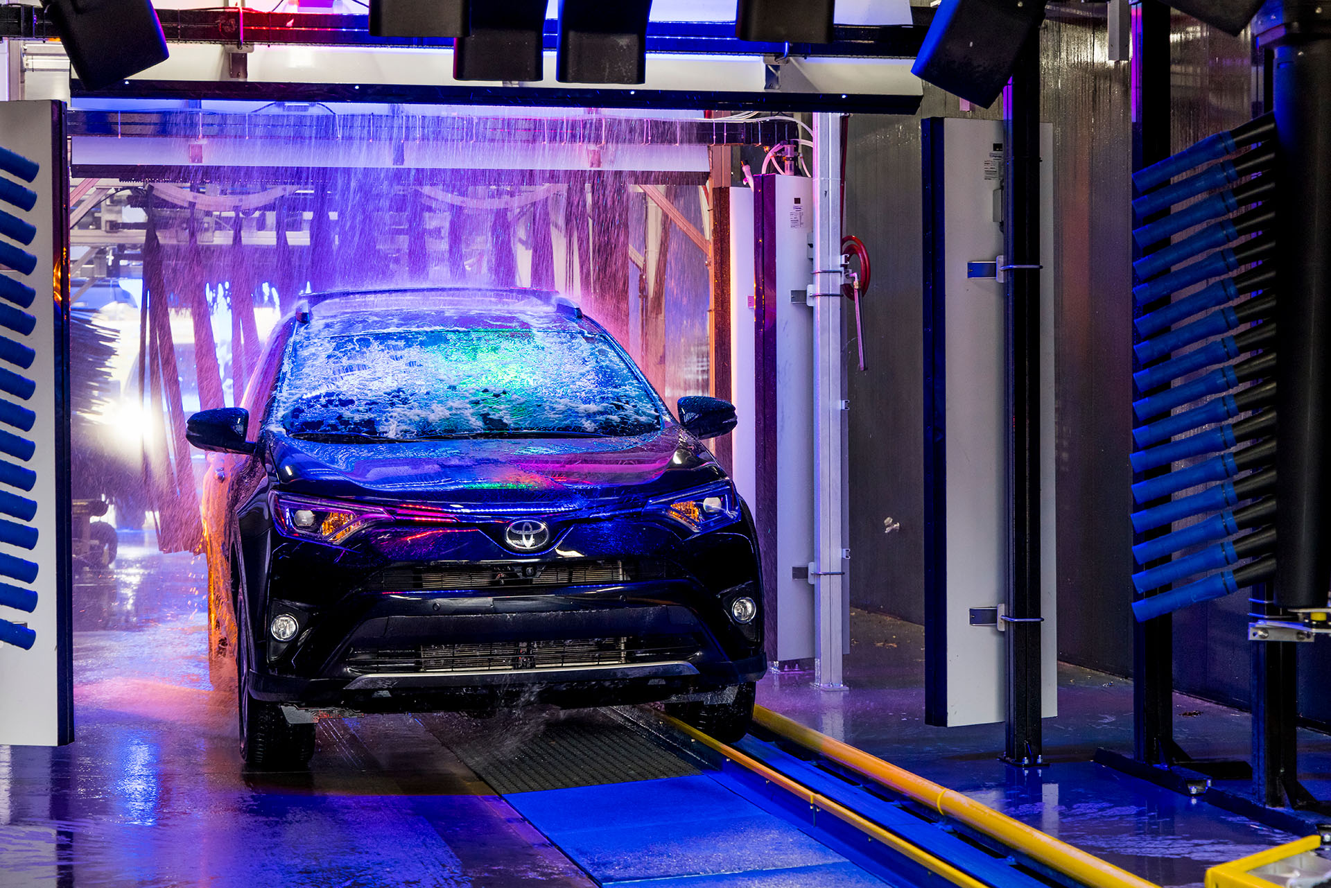 Black vehicle receives a spotless rinse in Big Dan's soft-touch automatic car wash, pulled along a track and illuminated by neon lights